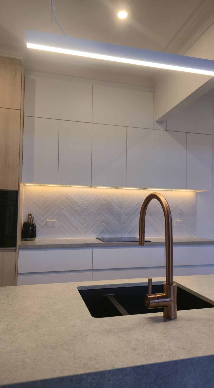 Close view of kitchen cabinetry, copper tapware and stone benchtop with under-cabinet lighting